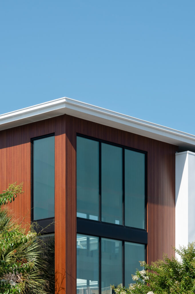 A modern beach house flanked by palm trees on a sunny blue-sky day.