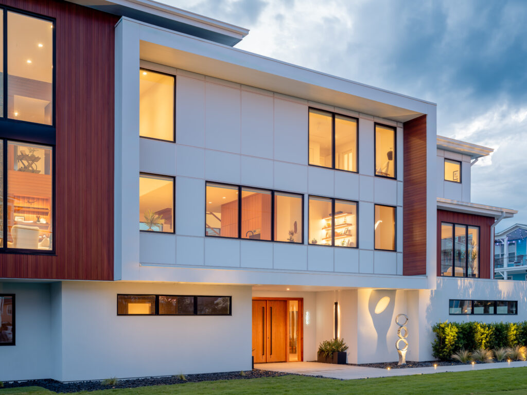 Side angle photograph of modern-coastal home lit from within at sunset.