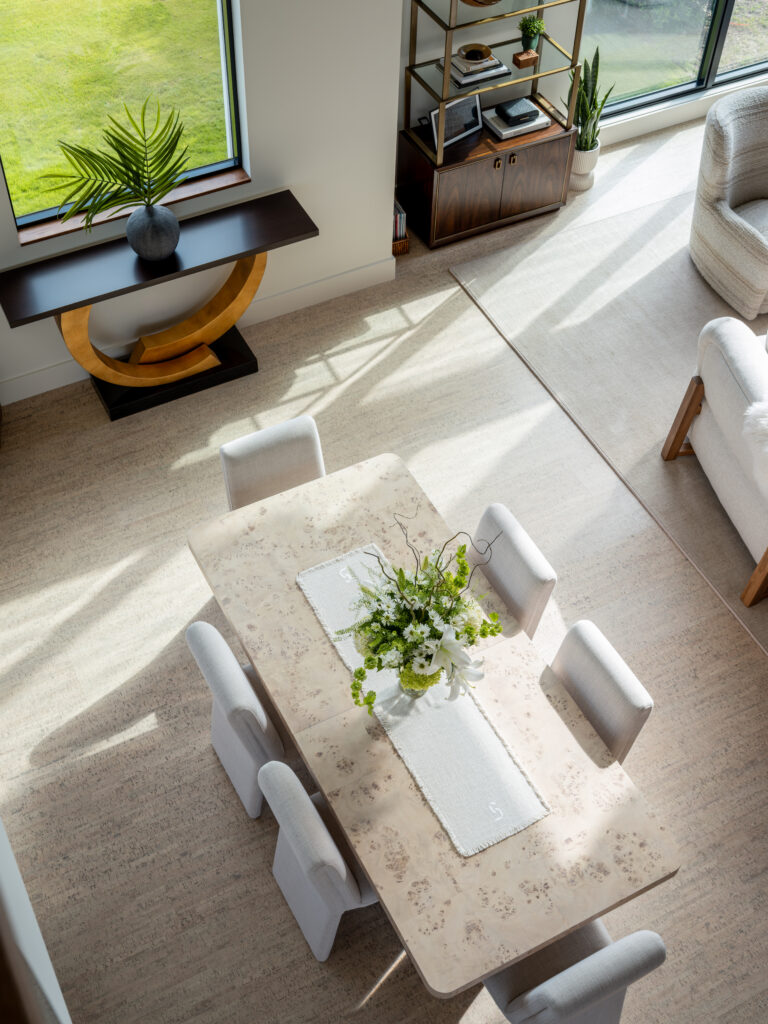 The view from the second floor to the first floor in this modern, coastal build in Carolina Beach, NC shows us beautiful light from the towering windows, modern and unique furniture, and an artistic flower arrangement.