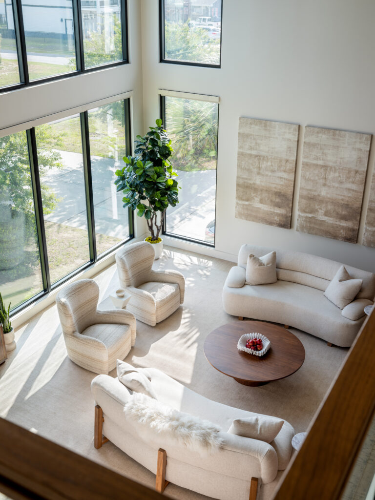 A bright, open living space defined by curved couches, a low, round coffee table, and two armchairs. The focal point (unseen) is a floor to ceiling dekton fireplace.